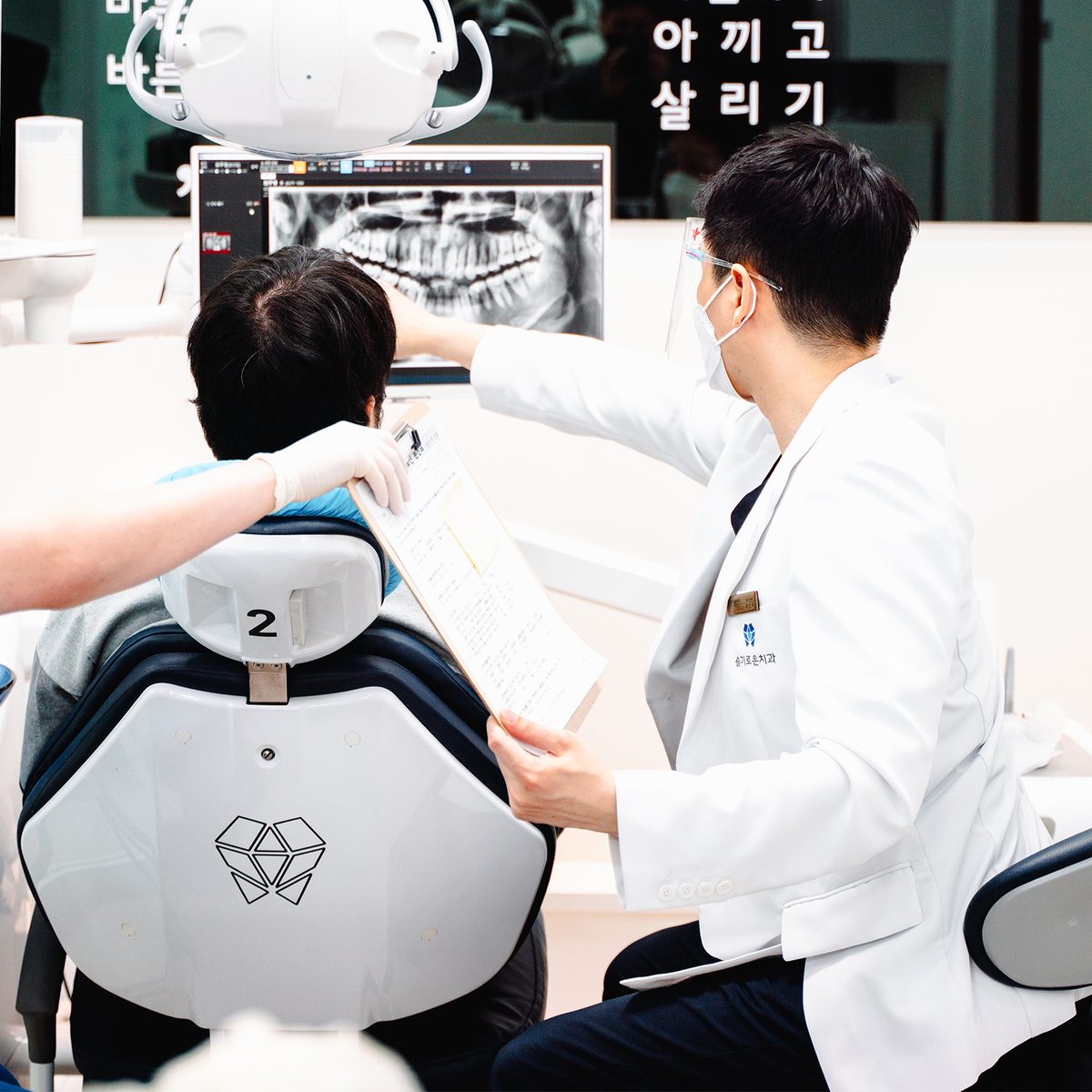 진료 의자 옆에서 모니터의 파노라마 방사선 영상을 가리키며 설명하는 슬기로운치과 진료진